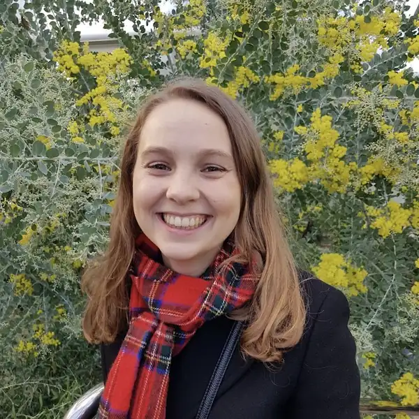 Photo of person smiling in front of green and yellow plants.