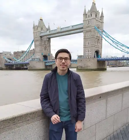 Photo of person smiling next to the River Thames in front of Tower Bridge.